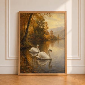 May include: A framed landscape painting depicting two white swans swimming on a calm lake. The scene features golden autumn trees along the shoreline, soft light reflecting on the water, and distant mountains under a hazy, warm-toned sky.