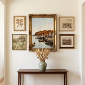 May include: A gallery wall arrangement featuring five framed artworks surrounding a central large gold-framed painting of a harbor with boats. Below, a light green ceramic vase holds dried wheat stalks on a dark wood console table.