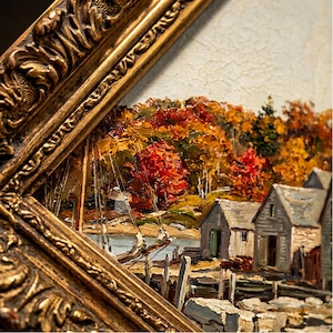 May include: An oil painting in a thick, ornate gold frame depicting a coastal scene with grey wooden sheds, a small boat at a dock, and a dense forest with vibrant autumn foliage in shades of red, orange, and yellow under a pale sky.