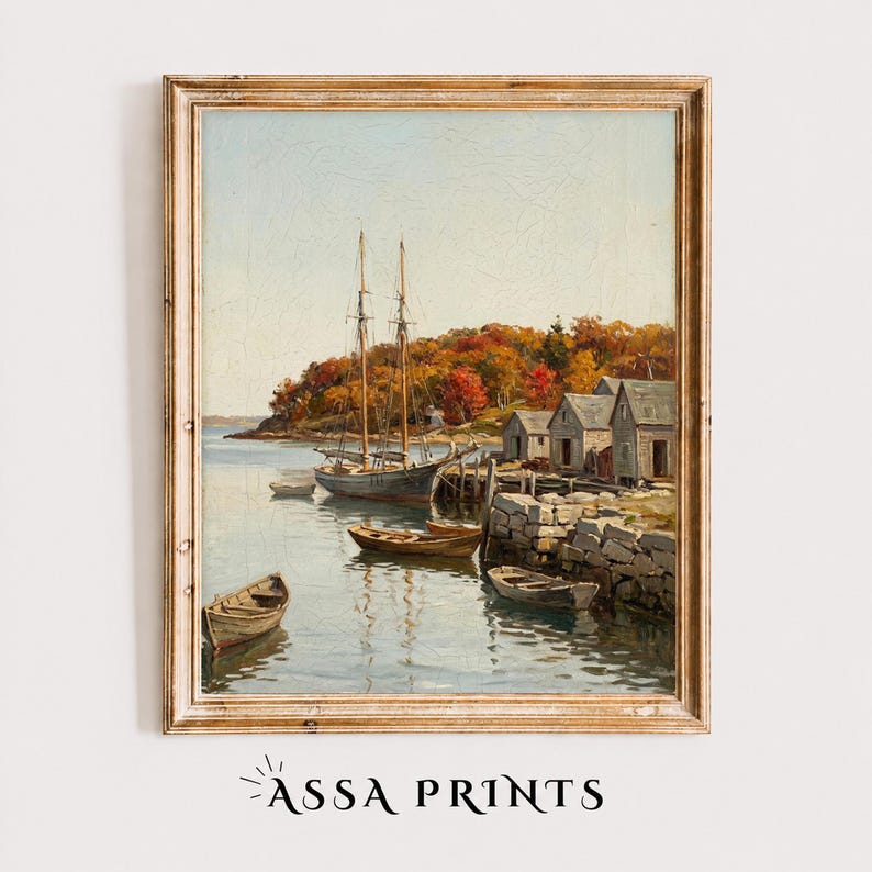 May include: A framed oil painting print depicting a coastal harbor scene with a sailboat, several small rowboats, and wooden buildings along a rocky shoreline. The landscape features trees with autumn foliage in shades of orange, red, and yellow.