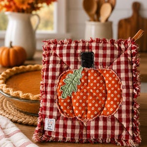 May include: A square quilted potholder featuring a red and white gingham pattern with a frayed edge. The center displays an orange pumpkin with white polka dots, a green leaf, and a black stem. A small white fabric tag reads I Love To Sew Becky.
