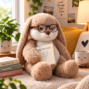 Pode incluir: Um peluche de coelho castanho-claro com orelhas compridas e barriga branca, usando óculos com padrão de tartaruga. O coelho segura uma pequena placa retangular que diz: OK, REALLY. Small steps make big changes. Nariz castanho e expressão séria.