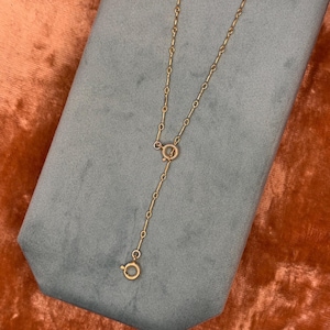 May include: A gold-toned metal necklace extender featuring a series of small, elongated bar links connected by circular jump rings. The chain includes a circular spring ring clasp at one end and a matching circular ring at the other end.