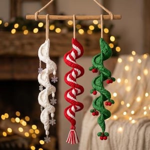 May include: Three hanging spiral ornaments suspended from a wooden rod. The left is white with silver snowflake charms, the center is red and white striped with a tassel, and the right is green with small red berry clusters attached throughout.