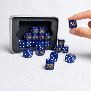 Peut inclure: Un ensemble de dés bleus à six faces avec des points blancs et un emblème de fer à cheval doré sur une face. Plusieurs dés sont rangés dans une boîte de rangement métallique rectangulaire avec un insert en mousse noire.