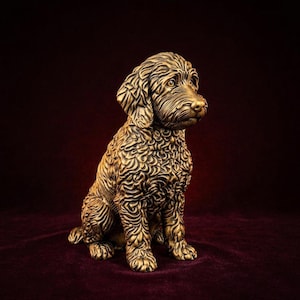Könnte beinhalten: Eine bronzefarbene Skulptur eines sitzenden Hundes mit lockigem, strukturiertem Fell. Die Figur zeigt detaillierte Fellmuster, Schlappohren und einen aufmerksamen Gesichtsausdruck, der an einen Doodle oder Retriever in aufrechter Haltung erinnert.