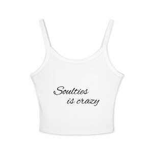 May include: A white sleeveless crop top with thin shoulder straps and a scoop neckline. The centre of the garment features the black text "Soulties is crazy" written in a cursive script font. The design is centred on the front of the shirt.