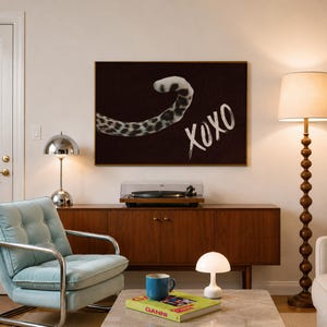 May include: A rectangular wall art print featuring a dark brown background with a leopard tail curving across the top left and the white hand-painted text XOXO in the bottom right corner, all enclosed within a thin gold-coloured metal frame.