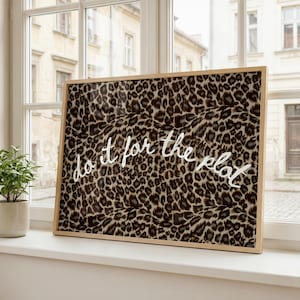 May include: A rectangular framed wall art piece featuring a brown, black, and tan leopard print pattern. The text 'do it for the plot' is written across the center in a white, cursive, handwritten-style font against the animal print background.