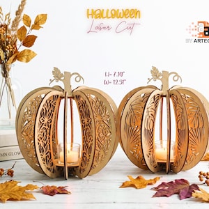 May include: Two light-coloured wooden pumpkin-shaped candle holders with intricate laser-cut patterns. Each features a central glass votive with a lit candle. Text reads HALLOWEEN Laser Cut and H= 18.03 cm W= 31.27 cm. The design includes leaf motifs.