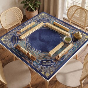 May include: A square mahjong table mat featuring a deep blue circular center surrounded by intricate gold and teal geometric patterns. The mat includes printed text detailing Charleston rules, with wooden tile racks and a small teapot present.