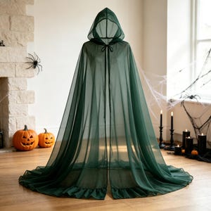 May include: A floor-length, sheer dark green hooded cloak made of lightweight fabric. The garment features a pointed hood, a simple tie closure at the neck, and a ruffled hemline that pools slightly on the floor, creating a flowing silhouette.