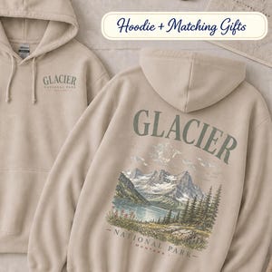 Pode incluir: Uma camisola com capuz cor de areia com um pequeno log&oacute;tipo do Glacier National Park no peito esquerdo e um gr&aacute;fico grande e detalhado nas costas que mostra uma cordilheira, um lago e pinheiros com o texto Glacier National Park Montana.