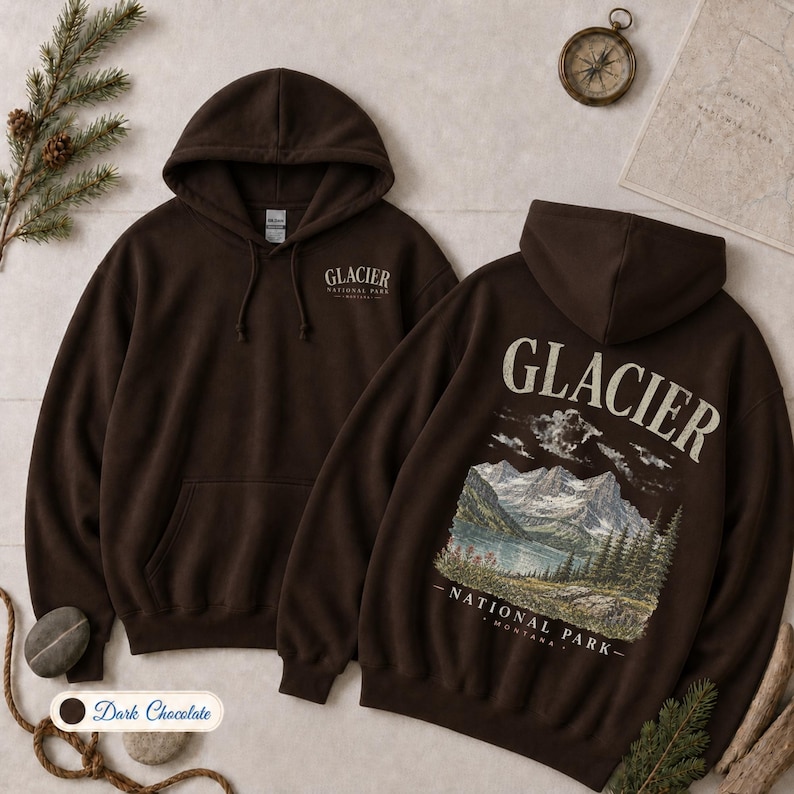 Pode incluir: Uma camisola com capuz castanho-escuro com um bolso frontal e capuz com cord&otilde;es. O peito apresenta o texto Glacier National Park. As costas exibem um gr&aacute;fico de montanhas, um lago e &aacute;rvores com o texto Glacier National Park Montana.