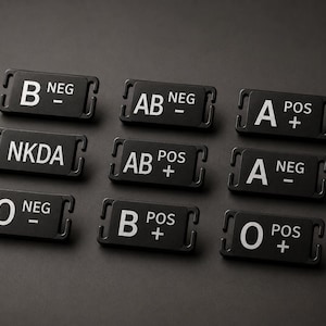 May include: A collection of nine rectangular black medical identification tags featuring white text. Each tag displays a specific blood type, such as B NEG, AB NEG, A POS, NKDA, AB POS, A NEG, O NEG, B POS, and O POS, with slots on each side for attachment.