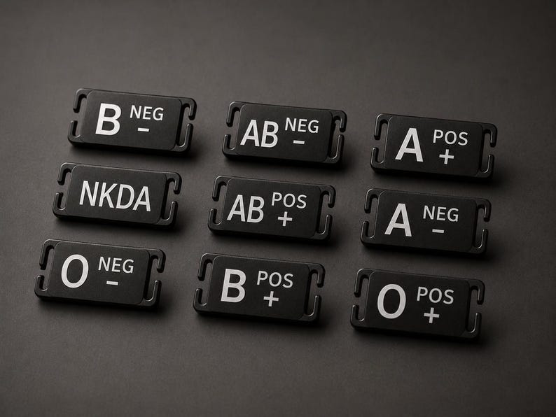 May include: A collection of nine rectangular black medical identification tags featuring white text. Each tag displays a specific blood type, such as B NEG, AB NEG, A POS, NKDA, AB POS, A NEG, O NEG, B POS, and O POS, with slots on each side for attachment.