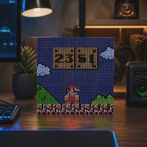 May include: A square pixel art display screen featuring a digital clock showing 23:51 in yellow text. The screen depicts a retro video game scene with a character in a red outfit, green hills, brown ground, and white clouds against a dark blue sky.