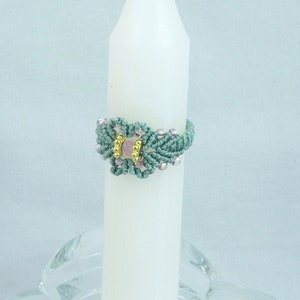 May include: A teal blue macrame ring with a pink and gold bead in the center.