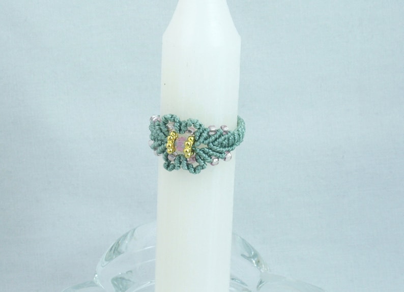 May include: A teal blue macrame ring with a pink and gold bead in the center.
