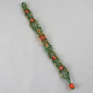 May include: A green and orange macrame bracelet with small beads. The bracelet is made using a knotting technique and features a decorative pattern.