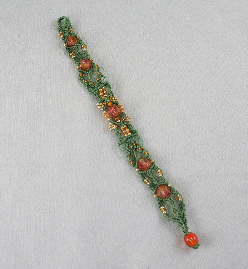 May include: A green and orange macrame bracelet with small beads. The bracelet is made using a knotting technique and features a decorative pattern.
