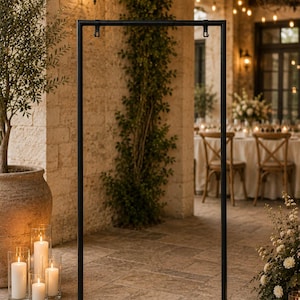 Puede incluir: Un soporte rectangular alto de metal negro con una base plana y dos pequeños ganchos sujetos a la barra horizontal superior. La estructura está construida con tubos de metal finos y uniformes, ofreciendo un diseño limpio y abierto.