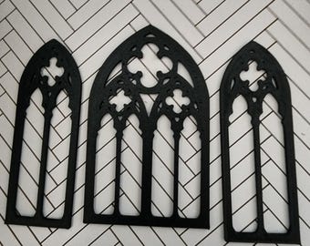May include: Three black, flat, decorative window frames featuring pointed gothic arches and intricate tracery patterns. The set includes one wider central frame and two narrower side frames, all constructed with a cutout design.