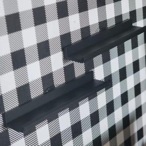 May include: Two matte black wall-mounted floating shelves with a narrow ledge design. Each shelf features a flat horizontal surface and a vertical back panel, providing a simple storage solution for displaying small items on a wall.