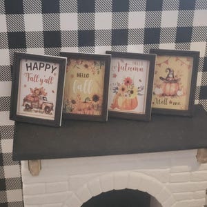 May include: Four rectangular framed signs with black borders featuring autumn-themed illustrations. The prints display pumpkins, sunflowers, a vintage truck, and a witch hat with text reading Happy Fall y'all, Hello fall, Hello Autumn, and Well me.