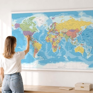 Può includere: Una grande mappa del mondo rettangolare da parete con uno sfondo oceanico azzurro e masse terrestri multicolori. La mappa mostra i nomi dei paesi, i confini e le etichette geografiche in nero, il tutto racchiuso in una cornice bianca.
