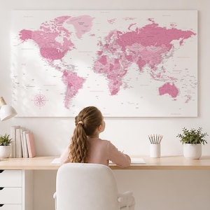 May include: A large rectangular wall map of the world featuring various shades of pink for landmasses against a white background. The map includes detailed geographical labels, country names, and a compass rose in the lower left corner.