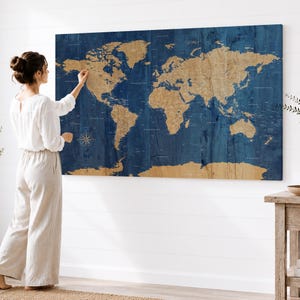 May include: A large rectangular wall art piece featuring a world map with tan-colored landmasses set against a deep blue, wood-grain textured ocean background. The map includes detailed geographical labels and a compass rose in the lower left.