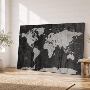 Peut inclure: Une grande œuvre d'art murale rectangulaire représentant une carte du monde imprimée sur un fond en grain de bois gris anthracite foncé. Les continents sont illustrés dans un ton gris clair avec des étiquettes géographiques visibles.
