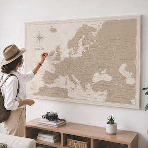 May include: A large, rectangular wall map of Europe in shades of beige and cream. The map features a compass rose in the upper left corner and the text "MAP OF EUROPE" printed below it. Country names and geographical borders are clearly visible.