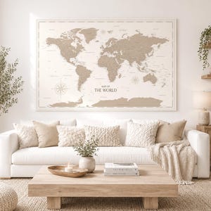 Puede incluir: Un gran cuadro rectangular de pared que muestra un mapa del mundo en beige y blanco con el texto "MAP OF THE WORLD" centrado bajo los continentes. El mapa incluye líneas costeras detalladas, nombres de países y dos rosas de los vientos.