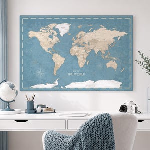 Peut inclure: Une impression murale rectangulaire représentant une carte du monde avec des continents beiges sur un fond bleu sourd. La carte inclut le texte "MAP OF THE WORLD" au centre et "ANTARCTICA" en bas, encadrée par une fine bordure blanche.