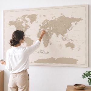 Op de afbeelding: Een grote rechthoekige wereldkaart met een beige achtergrond en zandkleurige continenten. De kaart bevat gedetailleerde geografische labels en de tekst MAP OF THE WORLD in een donker lettertype. Het is ingelijst met een dunne rand.
