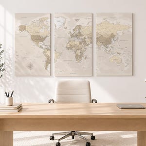 Può includere: Un set di tre quadri da parete raffigurante una mappa del mondo in tonalità neutre beige e marrone chiaro. Le tre tele rettangolari sono appese fianco a fianco, mostrando contorni geografici dettagliati, nomi di paesi e una rosa dei venti.