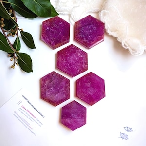 May include: Six hexagonal coasters in a vibrant magenta hue with a textured, crystalline surface. Each piece features a smooth, polished finish and a consistent geometric shape, arranged in a cluster on a white surface.