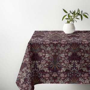 May include: A rectangular tablecloth featuring a deep burgundy background with a repeating botanical pattern of light pink flowers, muted blue accents, and intricate cream-colored foliage. A white ceramic vase with a green plant sits on top.