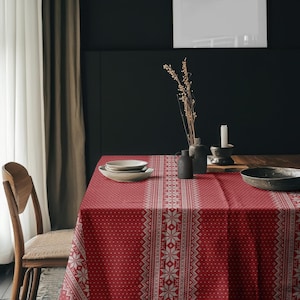 May include: A rectangular tablecloth featuring a deep red background with a repeating white Nordic-style pattern of snowflakes and geometric stripes. The fabric covers a table surface, accompanied by a stack of white bowls and a dark grey bowl.