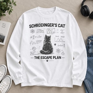 Puede incluir: Una sudadera blanca de manga larga con un estampado gráfico negro de un gato sentado de espaldas al espectador. El diseño incluye el texto "SCHRÖDINGER'S CAT" y "THE ESCAPE PLAN" junto a varias ecuaciones y diagramas de física.