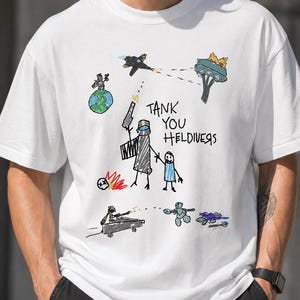 Peut inclure: Un t-shirt blanc arborant un motif coloré dessiné à la main. Le design comprend divers personnages, une planète, un véhicule et le texte "TANK YOU HELDIVERS" écrit dans une police manuscrite décontractée. L'illustration utilise des lignes simples.