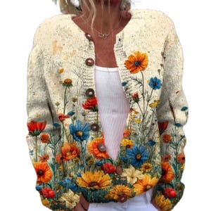 Puede incluir: Un cárdigan de punto color crema de manga larga con un estampado floral vibrante de flores silvestres rojas, naranjas, amarillas y azules. La prenda tiene un cuello redondo y un cierre frontal de botones en color marrón.