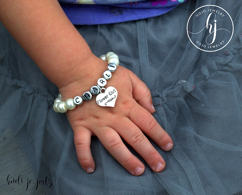 May include: A white pearl bracelet with a silver charm that says "Flower Girl" and the name "CHARLI".