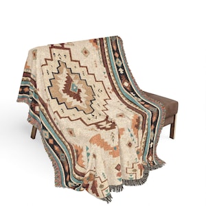 May include: A woven throw blanket featuring a cream-colored base with a geometric pattern in shades of rust, brown, black, and turquoise. The blanket has a textured appearance with fringed edges and a repeating diamond-inspired motif throughout.