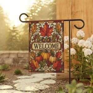 May include: A rectangular garden flag hanging on a black metal stand, featuring a stained glass style design with the word WELCOME in the center, surrounded by colorful autumn maple leaves, red berries, acorns, and three pumpkins in orange and yellow.