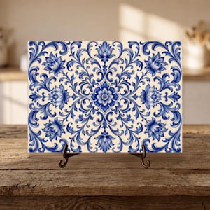 May include: A rectangular ceramic tile featuring a symmetrical blue and white floral pattern with intricate scrolling vines and leaves. The tile is displayed on a black metal stand, showcasing a detailed botanical design across its entire surface.