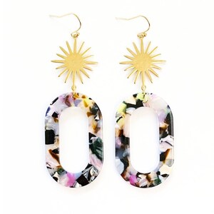 May include: A pair of long, dangling earrings with a gold starburst charm and a large oval-shaped pendant made of colorful, speckled resin.