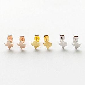 May include: Three pairs of Texas-shaped earrings in gold, rose gold, and silver.